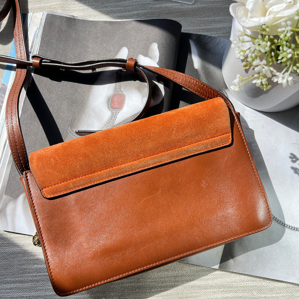 Brown leather handbag on a textured surface with flowers in the background