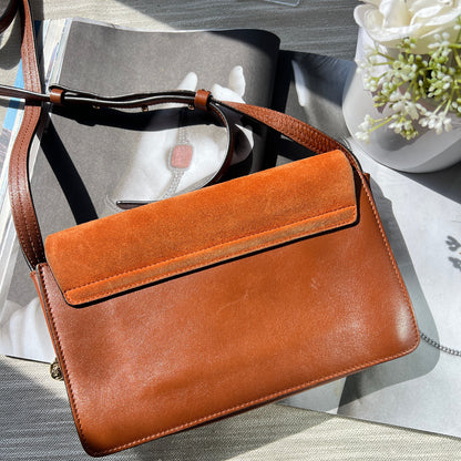 Brown leather handbag on a textured surface with flowers in the background