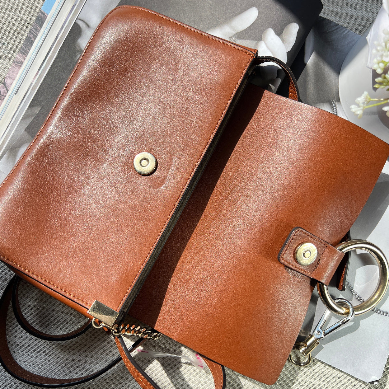 Brown leather handbag with gold hardware on a reflective surface