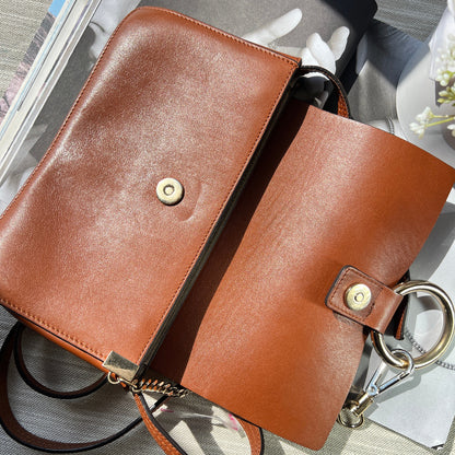 Brown leather handbag with gold hardware on a reflective surface