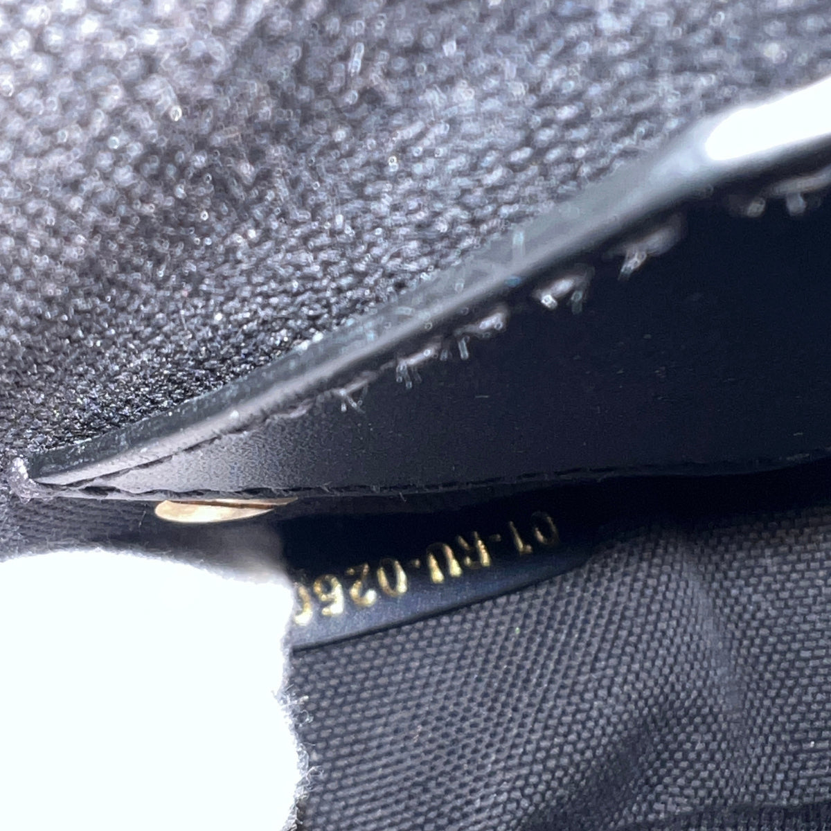 Close-up detail of a black textured fabric item with a black leather trim and gold stamped numbering.