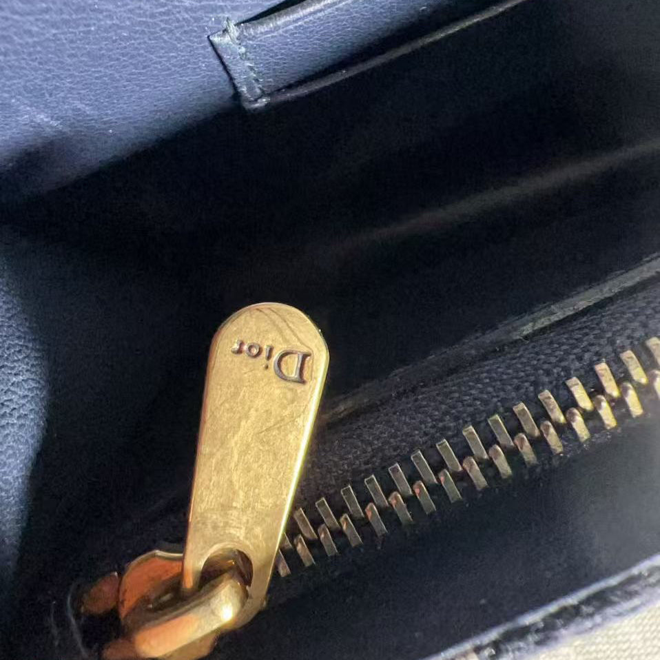 Close-up of a gold zipper pull on a black bag with visible brand name.