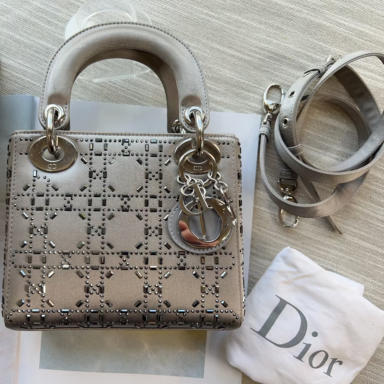 Designer handbag with decorative chain detail on a textured surface with a branded cloth.