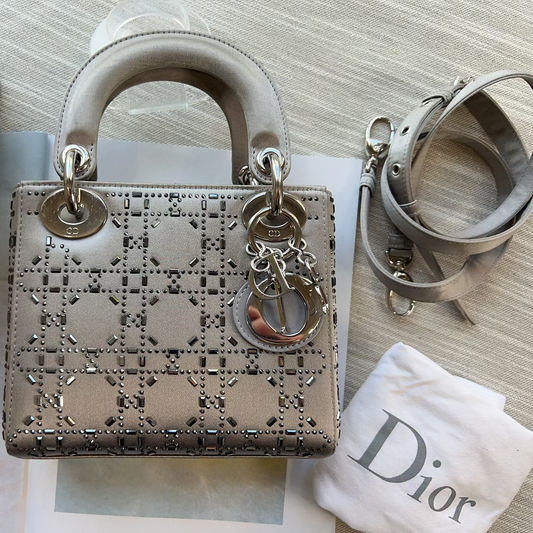 Designer handbag with decorative chain detail on a textured surface with a branded cloth.