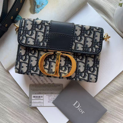 Dior Oblique monogram shoulder bag with a black leather strap and gold-tone hardware, displayed on a white surface with a Dior card and accessories.
