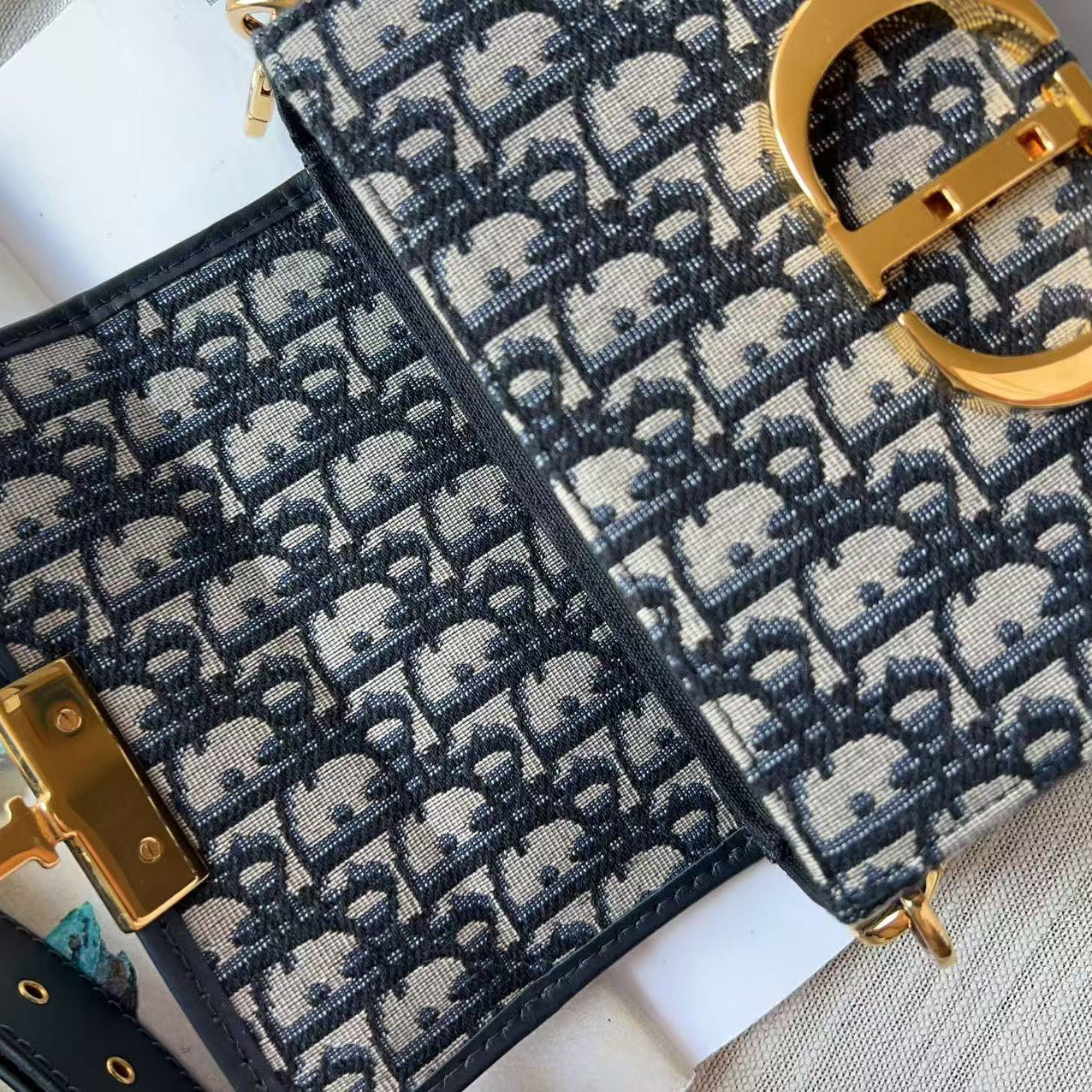 A close-up of a luxury handbag featuring the signature Dior Oblique monogram canvas in navy blue and beige, accented with gold-tone hardware.