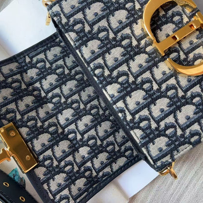 A close-up of a luxury handbag featuring the signature Dior Oblique monogram canvas in navy blue and beige, accented with gold-tone hardware.