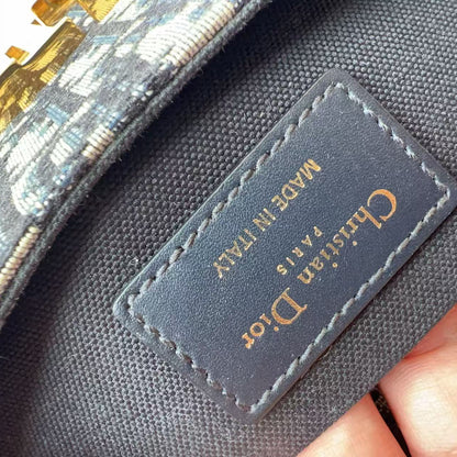 Close-up of a Christian Dior handbag showing the interior canvas lining and a stitched black leather brand label with gold lettering, held by a hand.