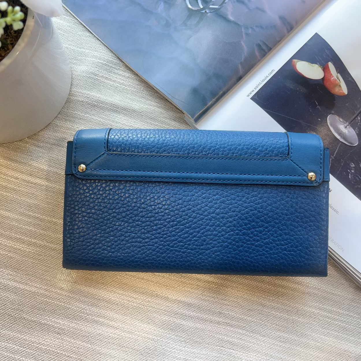 Blue wallet on a wooden surface with a plant and magazine in the background