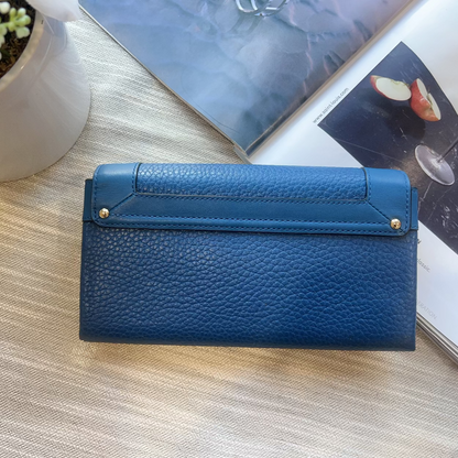 Blue wallet on a wooden surface with a plant and magazine in the background