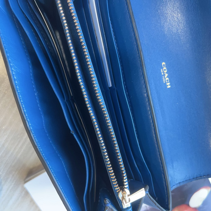 Blue Coach wallet with a visible brand logo on a light wooden surface.