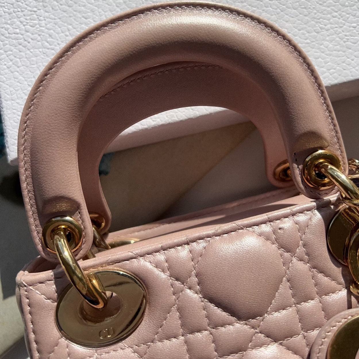 Close-up of a pink quilted handbag with gold hardware on a white background with 'Dior' branding.