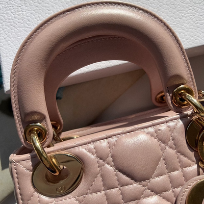 Close-up of a pink quilted handbag with gold hardware on a white background with 'Dior' branding.