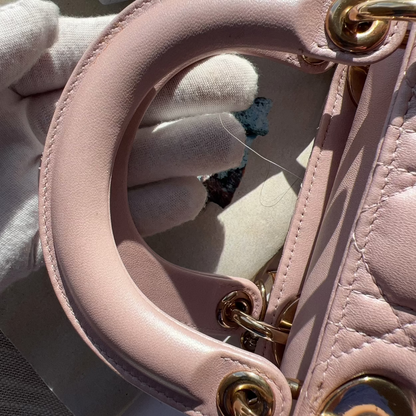 Close-up of a pink handbag handle with gold hardware, held by a gloved hand.