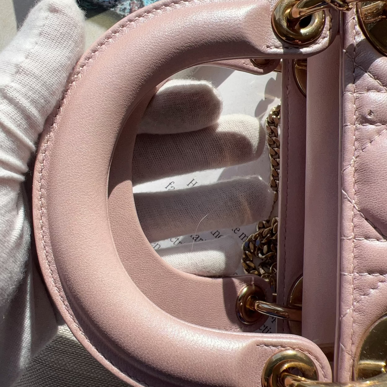 Close-up of a pink handbag with gold hardware held by a gloved hand.