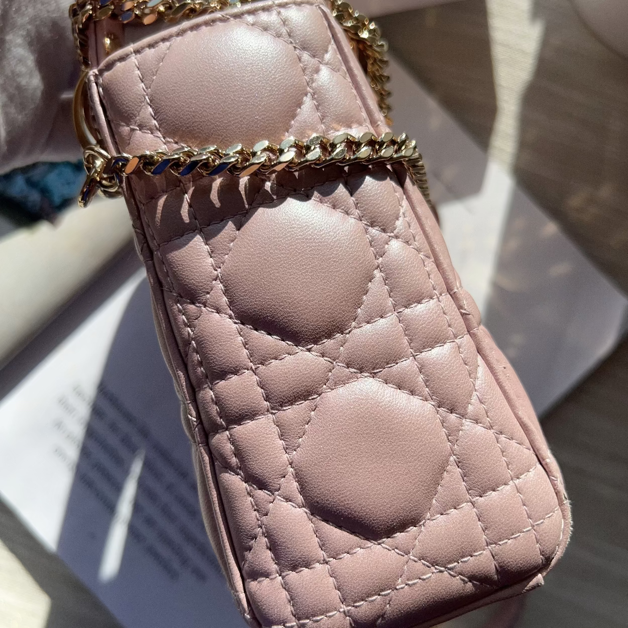 Pink quilted phone case with gold chain held by a hand