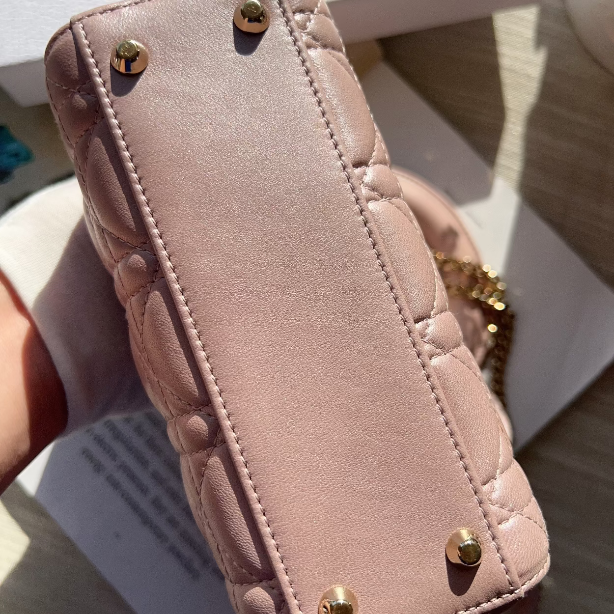 Pink quilted phone case with gold accents held by a hand on a light background