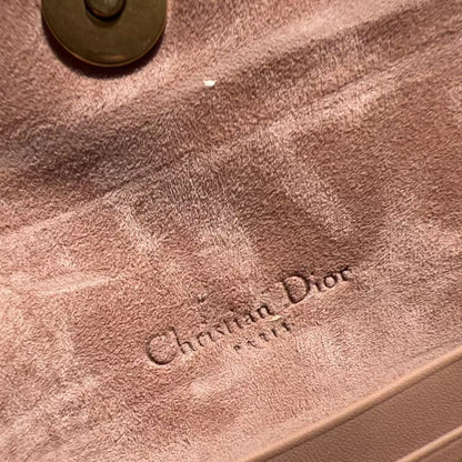 Close-up of a Dior handbag interior in dusty pink suede or velvety material, with the embossed Christian Dior logo visible and part of a gold-tone zipper at the bottom.