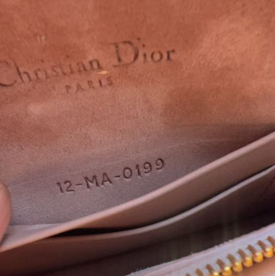 Close-up of a Christian Dior wallet or pouch interior in a warm tan leather, showing the embossed Christian Dior PARIS logo and the model number 12-MA-0199, with a gold zipper partially visible at the bottom.