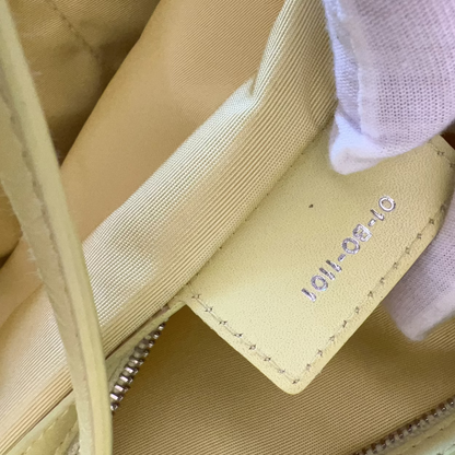 Close-up of a beige shoe with a brand label being held by a gloved hand.