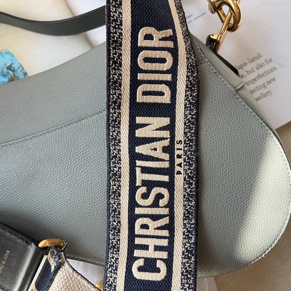 Gray handbag with a Christian Dior strap on a light surface.