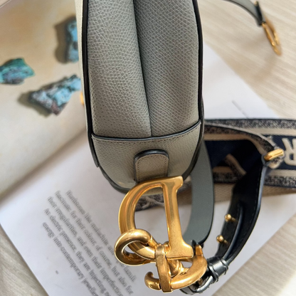 Gray handbag with a gold clasp on a surface with papers and a pen.