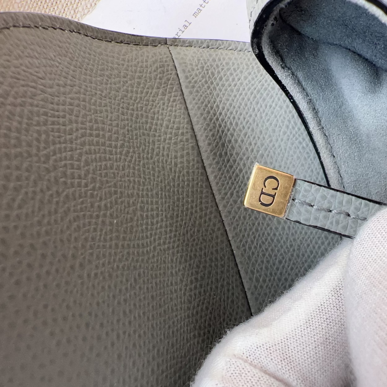 Close-up of a textured gray leather bag with a gold tag, showing brand initials.