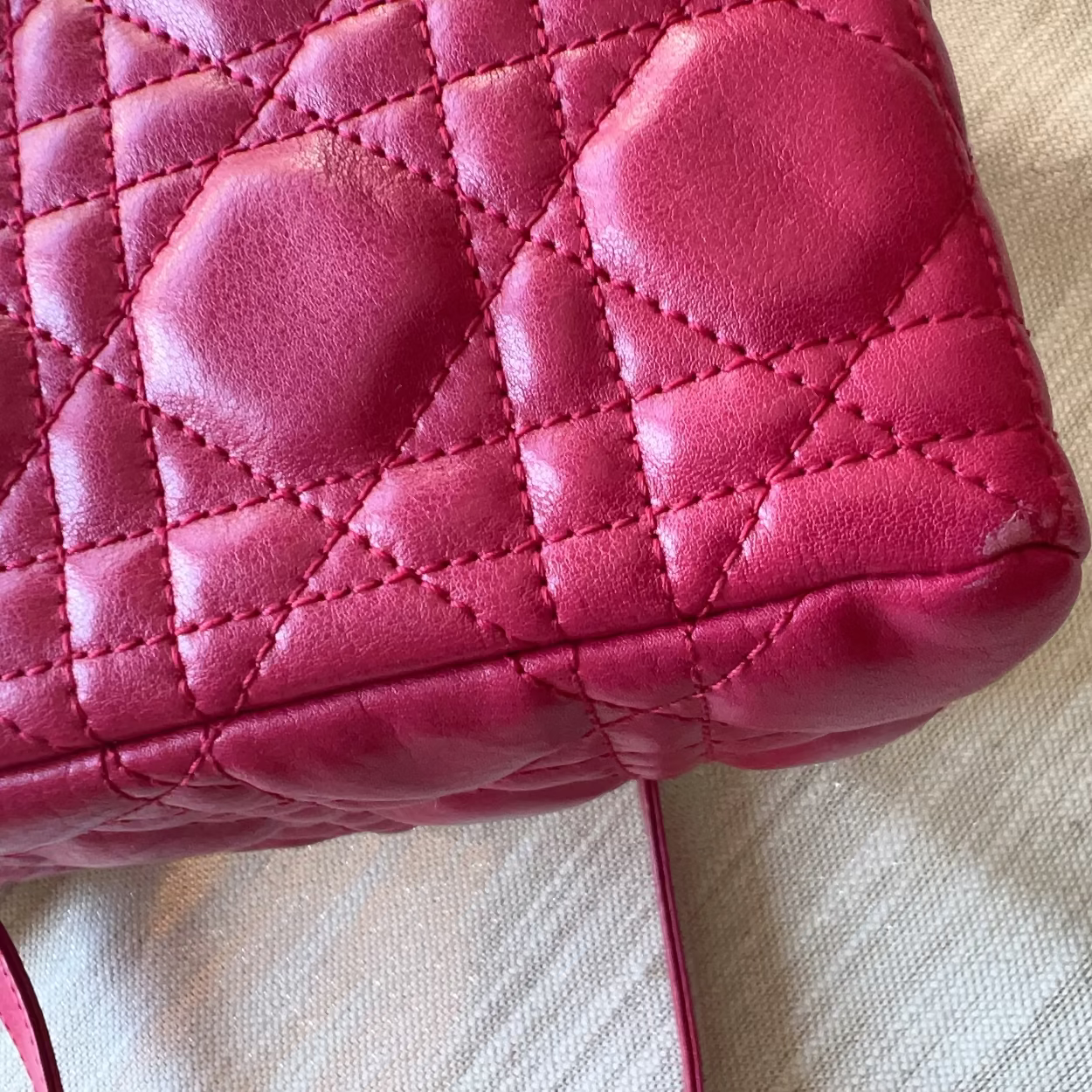 A close-up of a bright pink quilted leather handbag corner with diamond stitching, resting on a textured beige fabric surface.