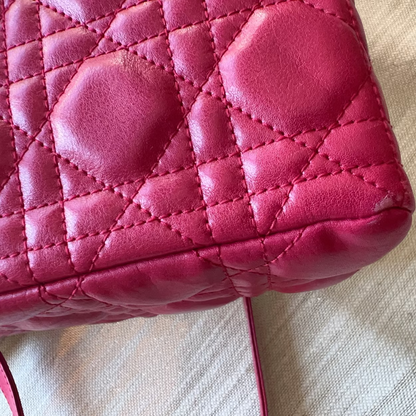 A close-up of a bright pink quilted leather handbag corner with diamond stitching, resting on a textured beige fabric surface.