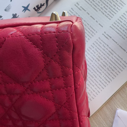 A close-up of a quilted pink leather handbag with gold-tone metal hardware, resting on an open book next to another book.