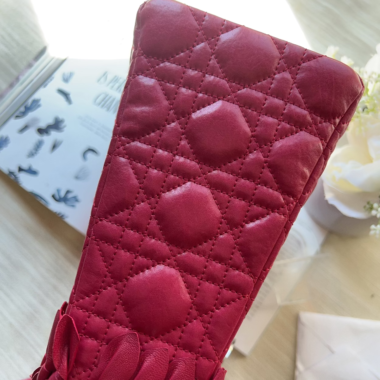 A close-up of a dark pink quilted leather shoulder bag with a diamond pattern and a fringed strap detail at the bottom, resting on a light wooden surface.