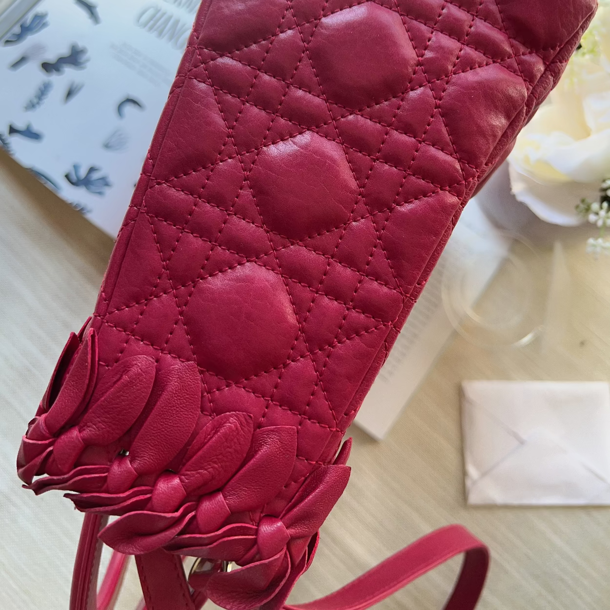 A close-up of a dark pink quilted leather shoulder bag with a diamond pattern and a fringed strap detail, resting on a light wooden surface.