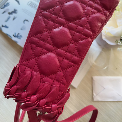 A close-up of a dark pink quilted leather shoulder bag with a diamond pattern and a fringed strap detail, resting on a light wooden surface.