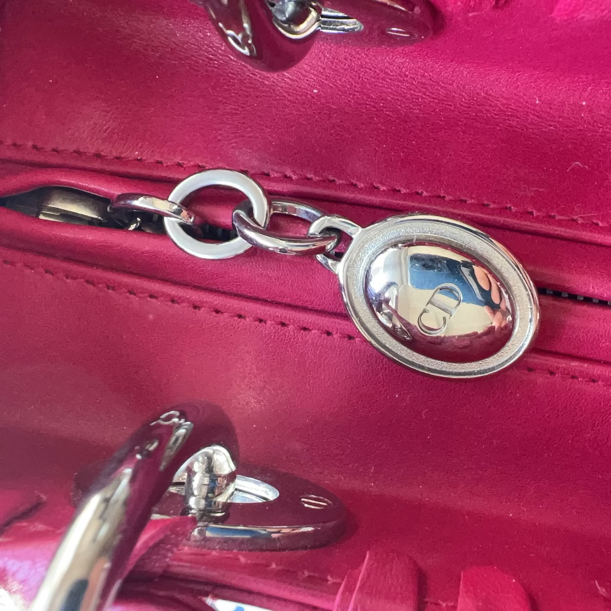 A close-up of a bright pink leather handbag showing a silver-tone metal zipper pull with a circular logo emblem.