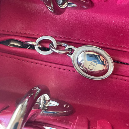 A close-up of a bright pink leather handbag showing a silver-tone metal zipper pull with a circular logo emblem.