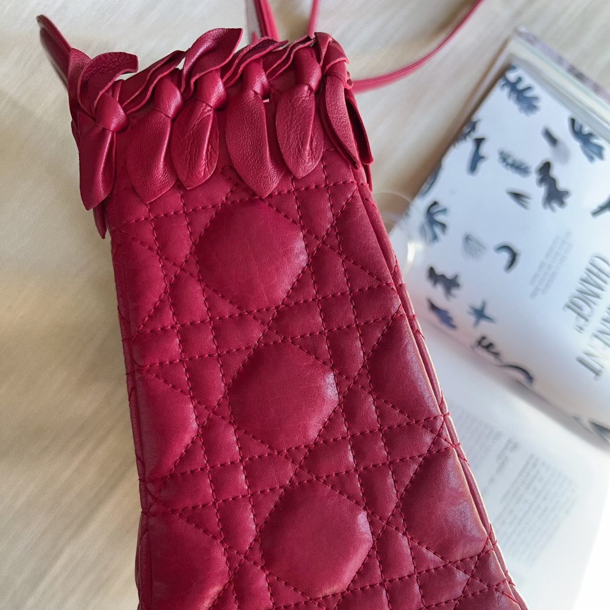 A deep red quilted leather pouch with a decorative ruffled top, styled on a light wood surface next to a magazine.