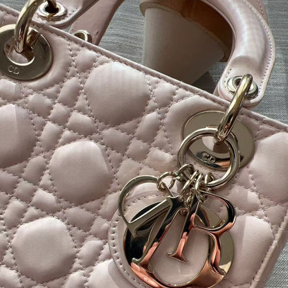 Close-up of a light pink quilted leather handbag with a large metallic rose gold and silver-tone Christian Dior 'CD' charm hanging from the handle attachment.