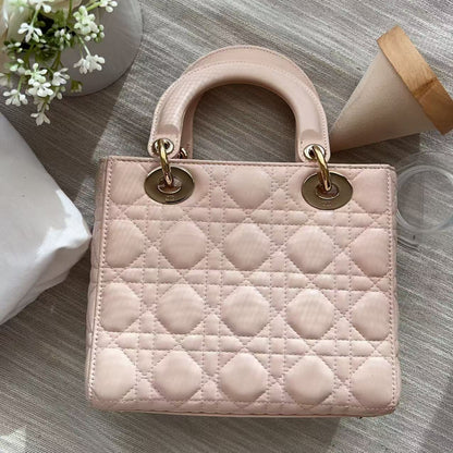 A light pink quilted leather handbag with top handles and gold-tone hardware, photographed from above on a gray wood-textured surface with decorative props.