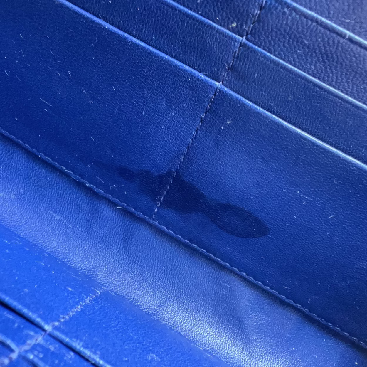 Close-up of a blue textured material with stitched paneling and a dark stain or wet spot visible near the center.