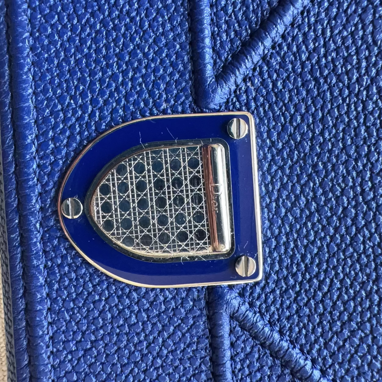 Close-up of a textured royal blue leather accessory featuring a prominent metallic silver and blue geometric logo clasp.