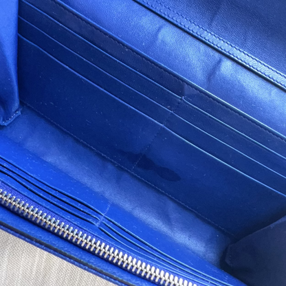 Close-up of the interior of a blue leather clutch or wallet, showing multiple card slots, a silver zipper, and a small dark stain on the inner surface.