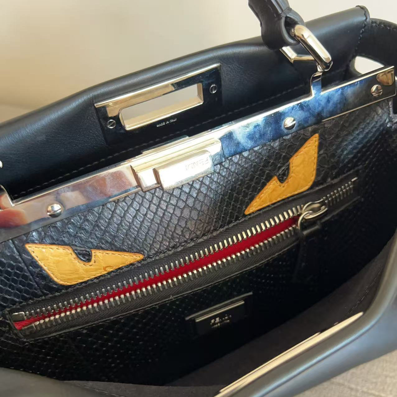 Close-up of a Fendi handbag interior showing the black textured leather inside, gold-toned metal hardware, a red zipper track, and the iconic gold eye logo patches on the black exterior.