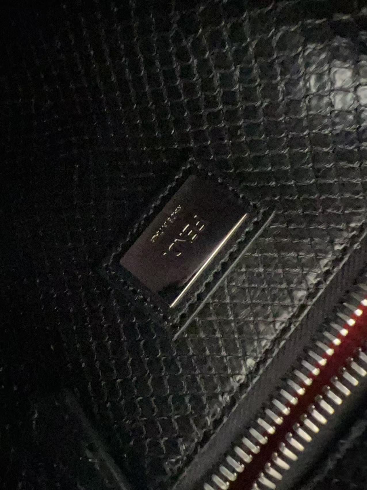 Close-up of a black textured leather wallet or clutch with a metallic silver-tone 'F. R.
