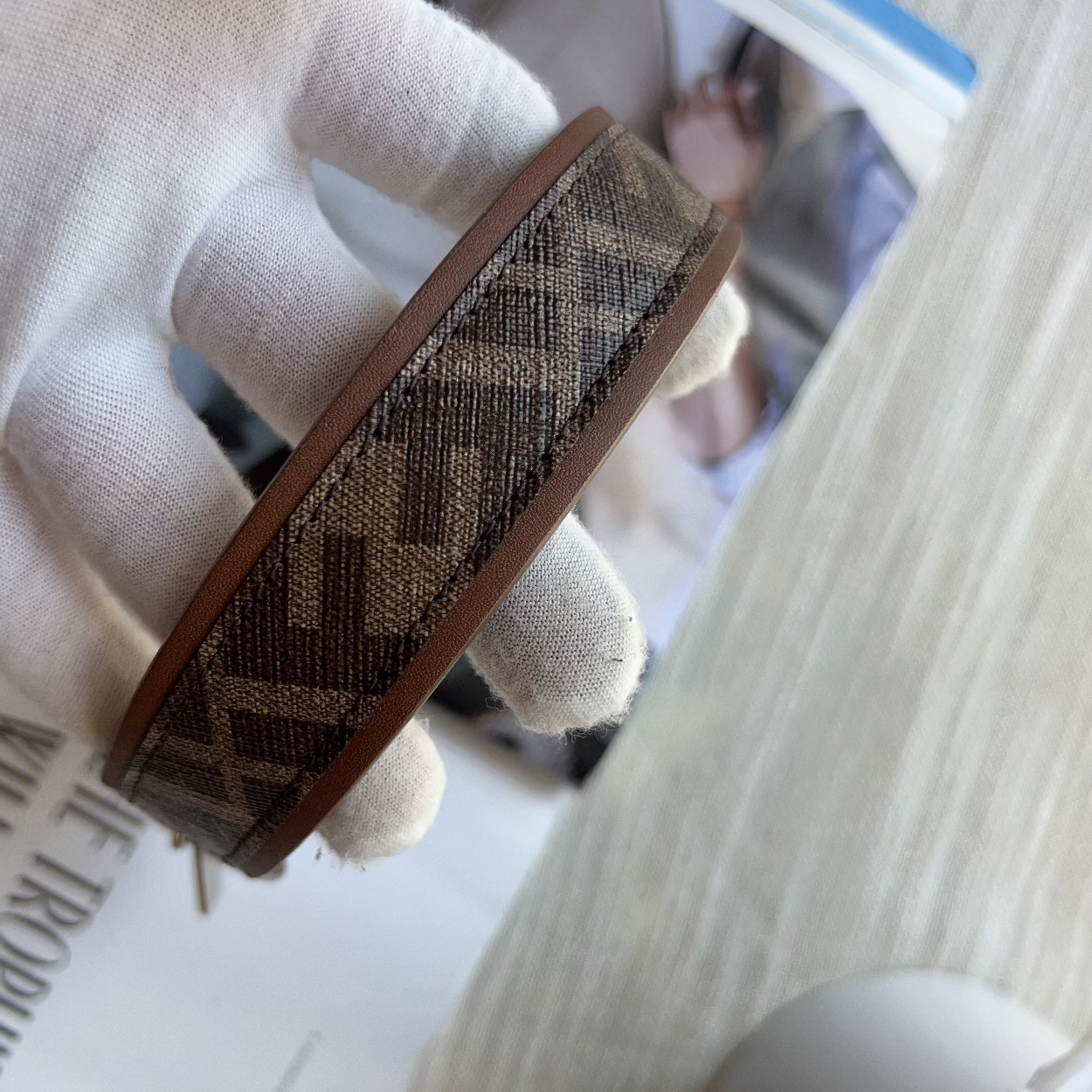 Textured belt with a pattern held by a gloved hand on a blurred newspaper background