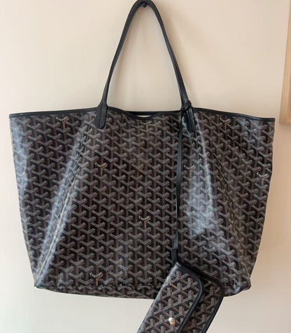 A Goyard black and brown monogram tote bag with matching wallet, hanging against a plain beige wall.