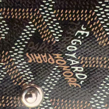 Close-up of a Goyard monogram canvas bag with black, beige, and white pattern, featuring the brand name 'Goyard Paris' and a silver metal snap button.