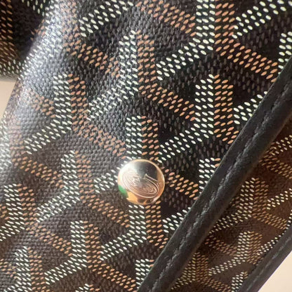 Close-up of a Goyard bag featuring the brand's signature chevron pattern in brown, beige, and black canvas, with a silver-tone metal snap button.