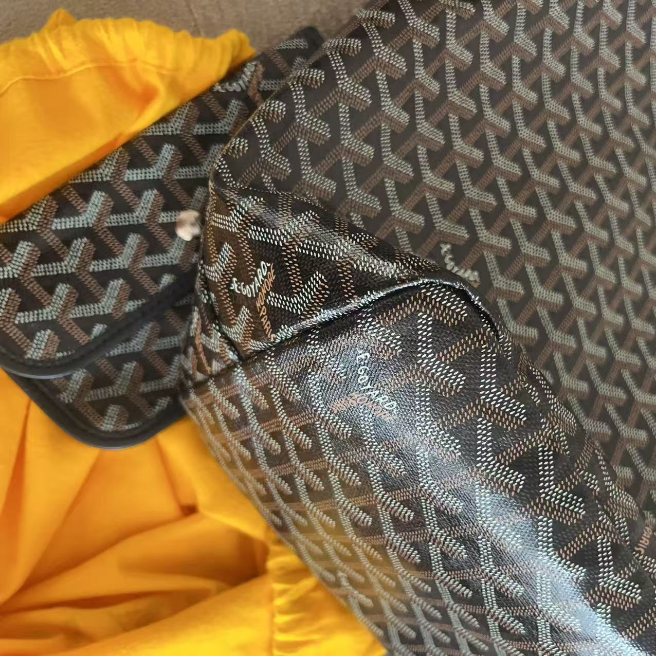 A Goyardine tote bag with its matching zippered pouch, displayed next to a bright yellow garment on a neutral surface.