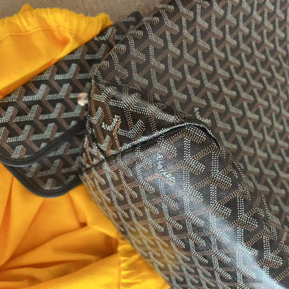 A Goyardine tote bag with its matching zippered pouch, displayed next to a bright yellow garment on a neutral surface.