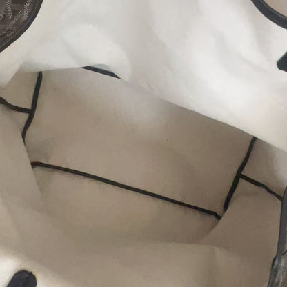 Close-up of the interior of a tote bag, showing a cream-colored fabric lining with black piping and a patterned gray and white side panel.